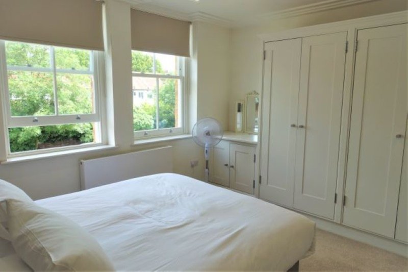 Bright bedroom with double bed, fitted wardrobes, fan and large windows overlooking greenery