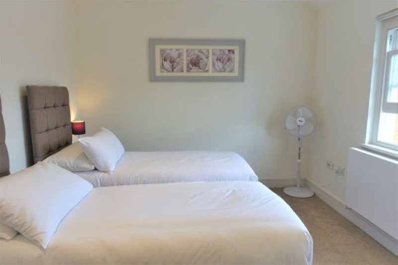 Bedroom with two single beds, brown headboard, white bedding, framed wall art and fan