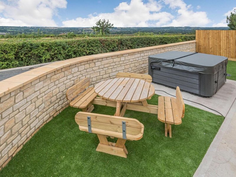Outdoor terrace with wooden picnic table, benches, hot tub, and countryside views
