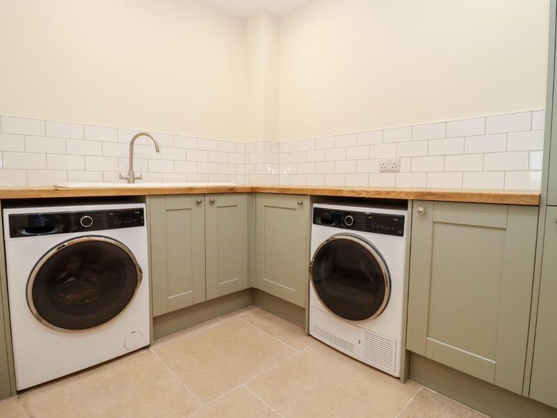 Laundry room with two white washing machines, wooden countertop, cream cabinetry and white subway tile