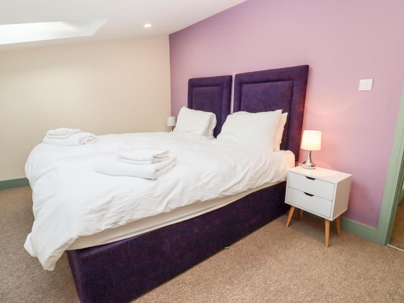 Modern bedroom with purple upholstered bed, white bedding, white nightstand, and pink accent wall