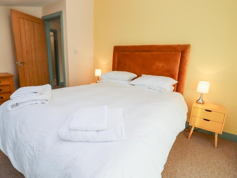 Bedroom with double bed, orange headboard, white bedding, wooden door and side tables