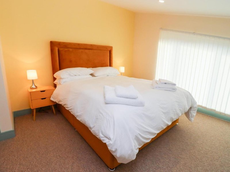 Bright bedroom with orange upholstered bed, white bedding, wooden nightstand and vertical blinds