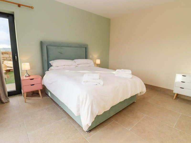 Modern bedroom with green upholstered bed, white bedding, wooden floor and bedside tables