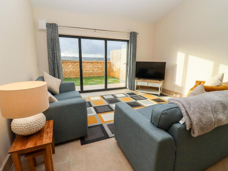 Modern living room with grey sofas, patterned rug, TV, and garden view through patio doors