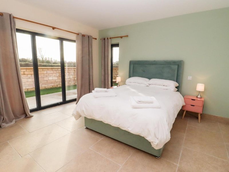 Spacious bedroom with double bed, green headboard, patio doors and garden view