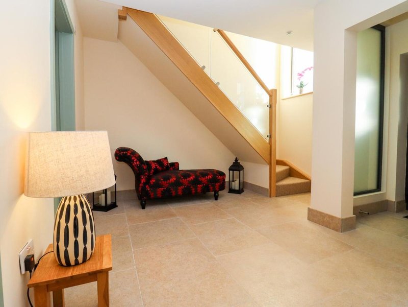Open-plan living space with wooden staircase, red patterned chaise lounge, table lamp and natural light