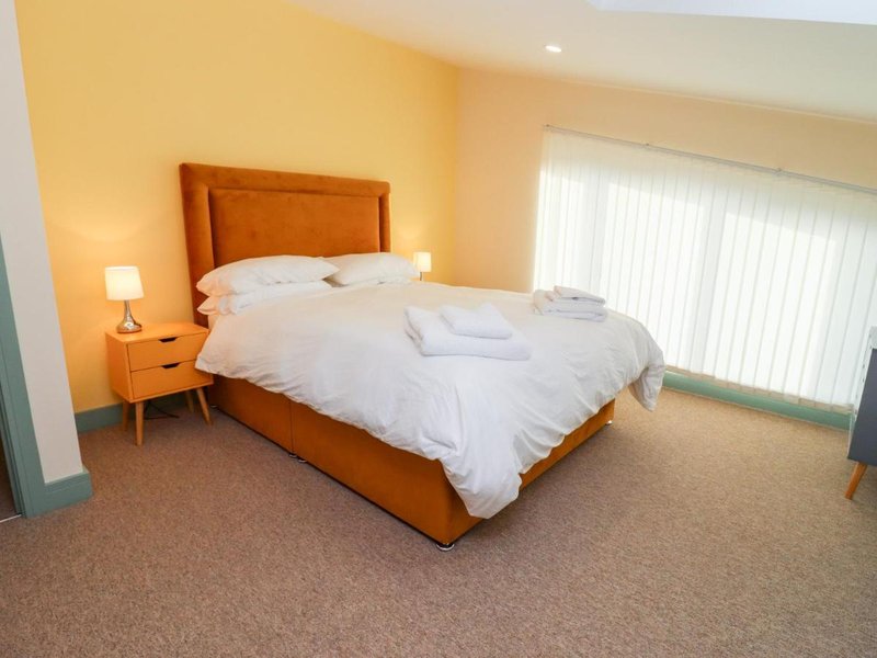 Bright bedroom with wooden bed frame, white bedding, orange headboard, and bedside table with lamp