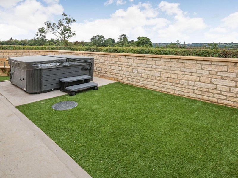 Outdoor patio area with hot tub, manicured lawn, brick wall, and countryside views