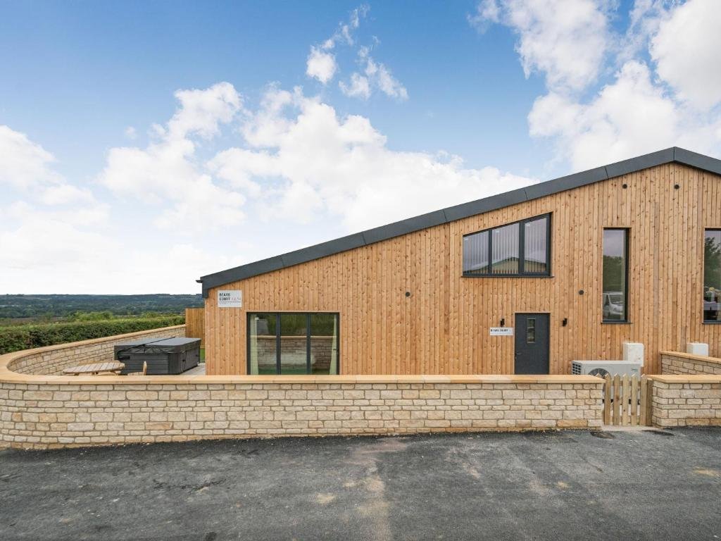 Modern wooden and stone house with large windows, driveway, and rural countryside views