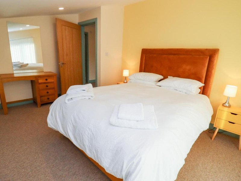 Spacious bedroom with double bed, orange headboard, wooden furniture, and yellow walls