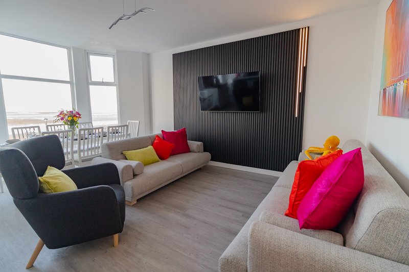 Bright living room with two sofas, armchair, wall-mounted TV, colorful cushions and natural light