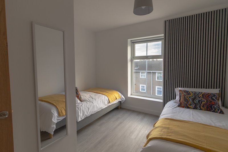 Bright twin bedroom with two single beds, yellow bedding, mirror, and large window with curtains