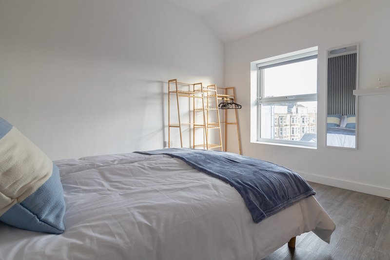 Bright bedroom with double bed, blue bedding, wooden ladder, and city window view