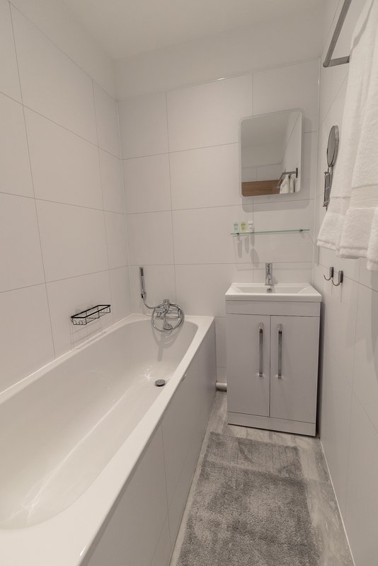 Clean modern bathroom with white tiles, bathtub, sink vanity, and mirror