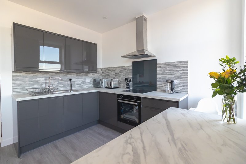 Modern kitchen with dark cabinetry, marble countertop, integrated oven and fresh flowers in vase