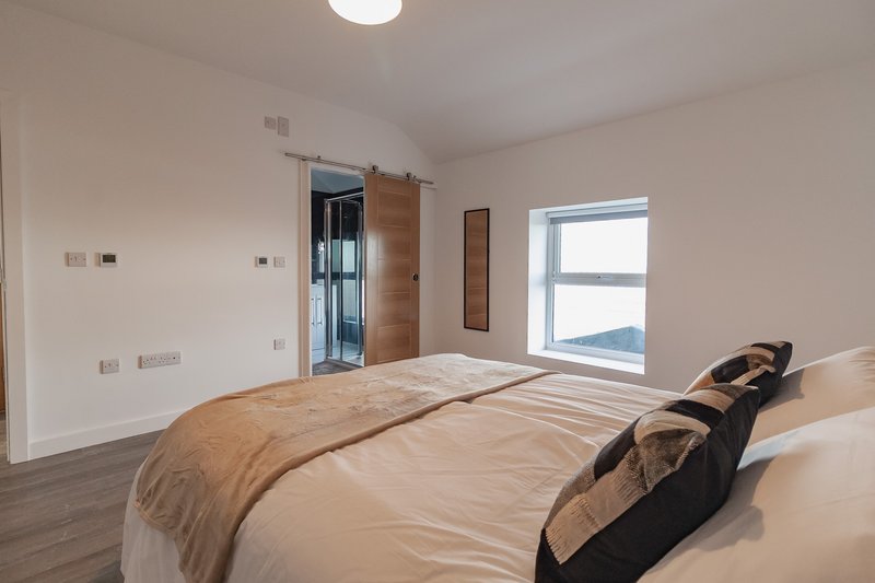 Bright modern bedroom with double bed, wooden sliding door wardrobe, and large window
