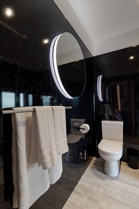 Modern bathroom with circular mirror, black wall, towel rail and white toilet