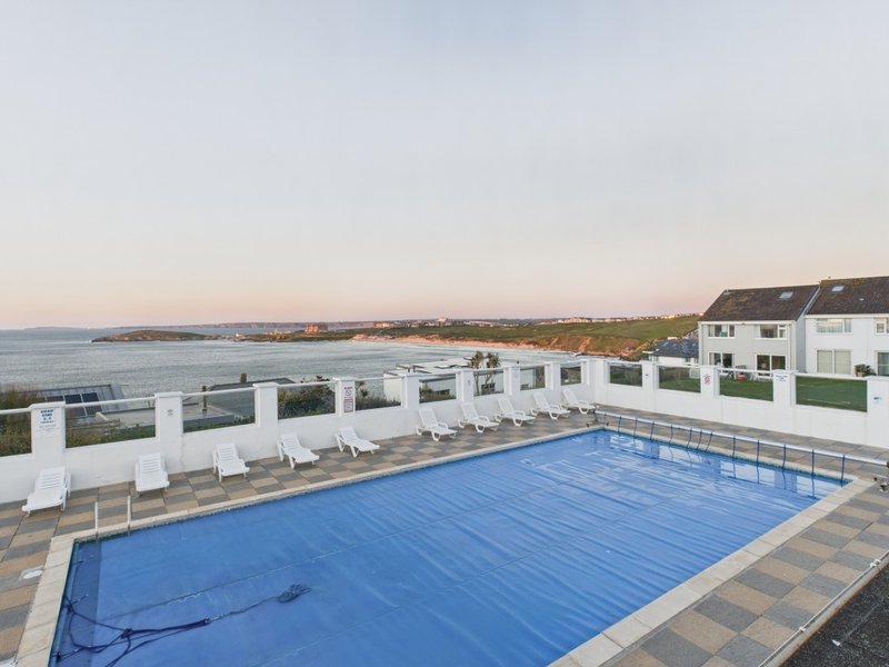Swimming pool with blue cover, white loungers, and coastal views at dusk