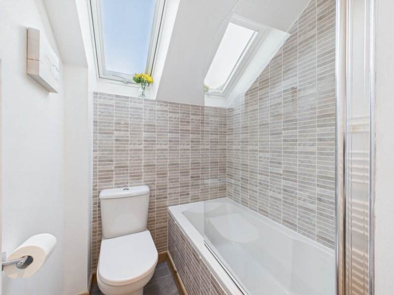 Modern bathroom with skylight, striped tile walls, white toilet, bathtub and shower