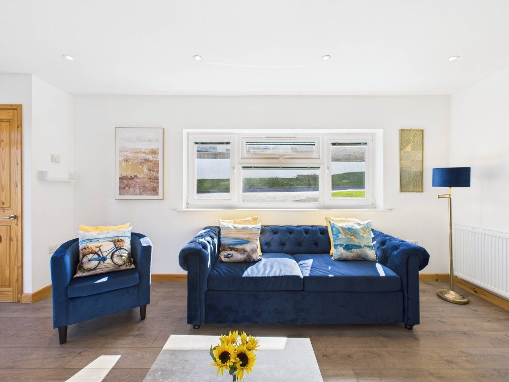 Bright living room with blue velvet sofa and armchair, wooden flooring, and landscape artwork