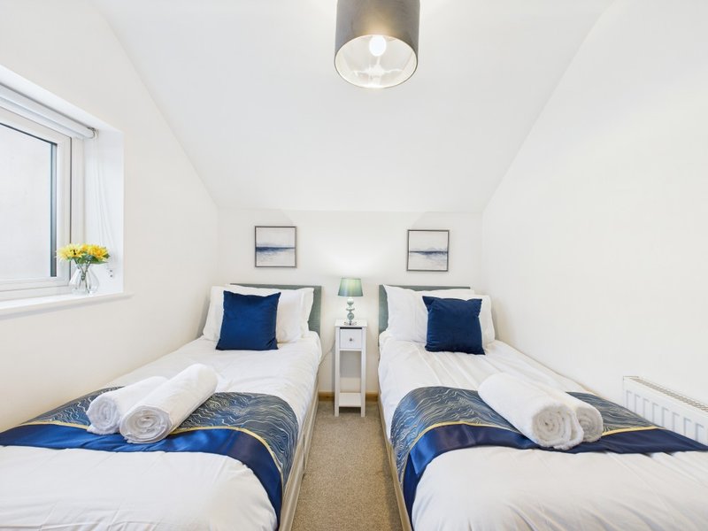 Twin bedroom with two single beds, blue bedding, white pillows, small window and ceiling light