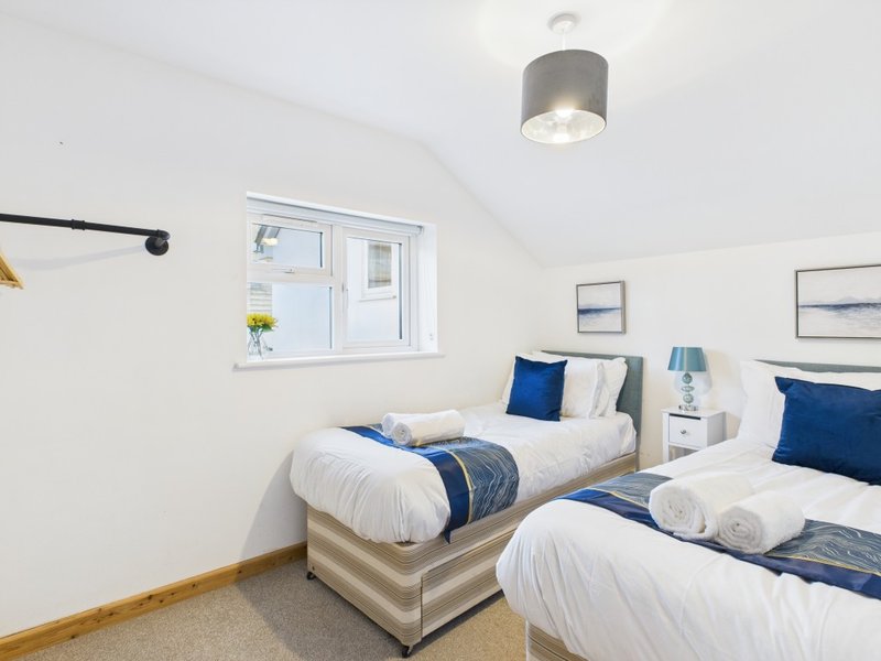 Twin bedroom with white walls, two single beds with blue accents, window and ceiling light