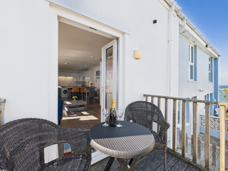 Coastal deck with wicker chairs, round table, and view into modern open-plan kitchen