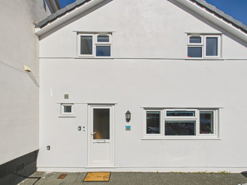 White rendered house exterior with front door, windows, and driveway approach