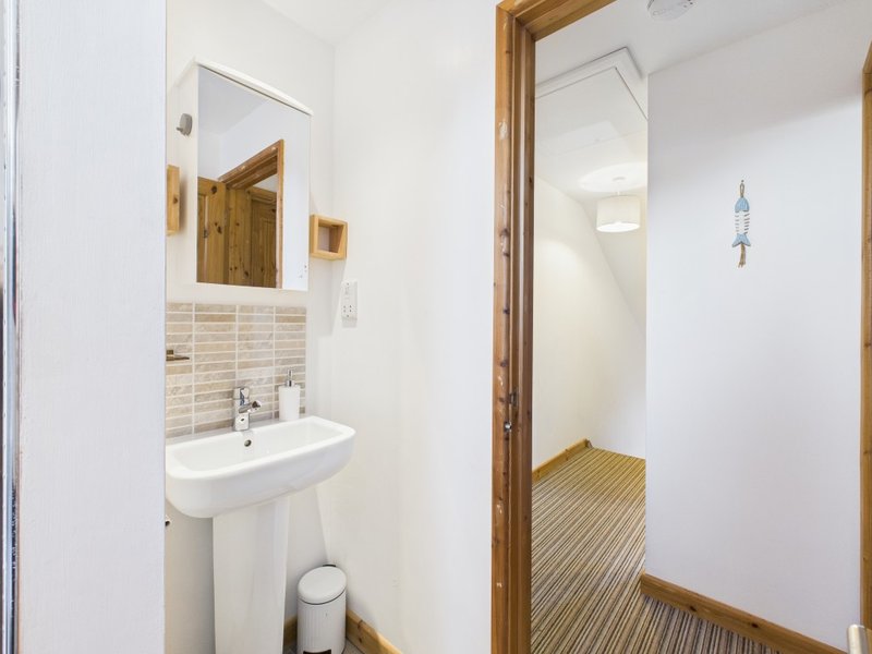 Compact bathroom with pedestal sink, tiled backsplash, wooden-framed mirror and adjacent wooden floored hallway