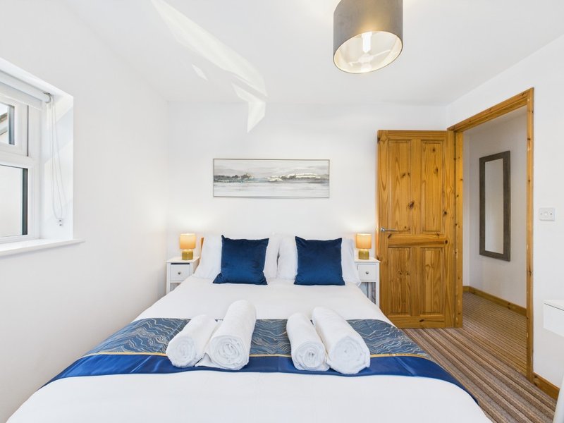 Modern bedroom with double bed, blue pillows, white bedding, wooden wardrobe and ceiling light
