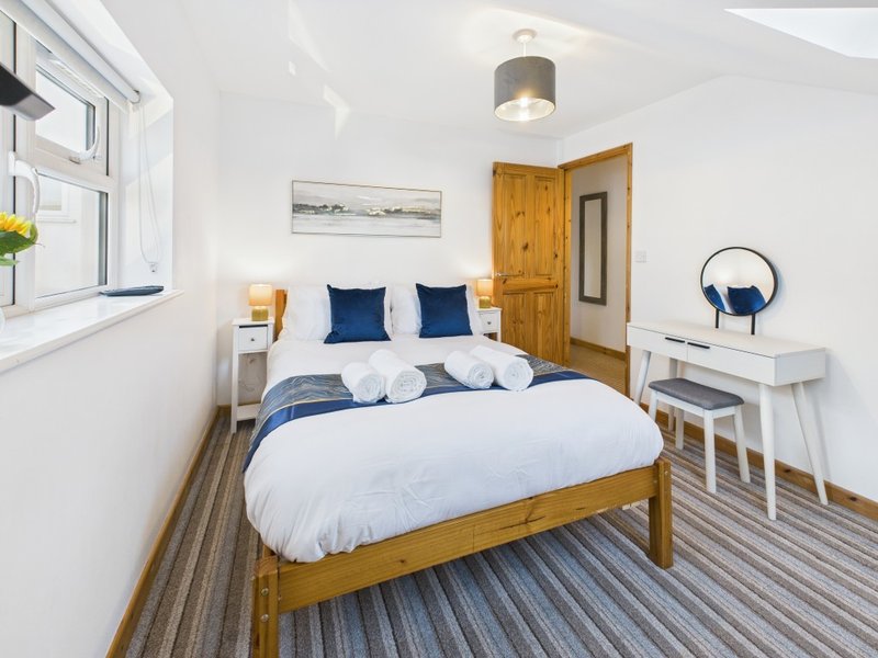 Bright bedroom with wooden bed, blue cushions, white bedding, wooden door and striped carpet