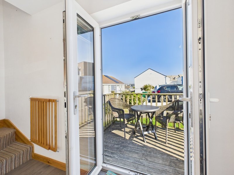 Open patio doors leading to wooden deck with outdoor furniture and neighborhood view