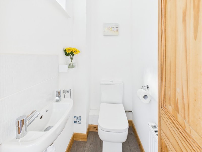 Compact bathroom with white toilet, sink, yellow flowers in vase, wooden door frame