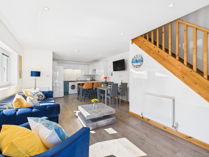 Open-plan living space with blue sofa, wooden staircase, kitchen area and dining table