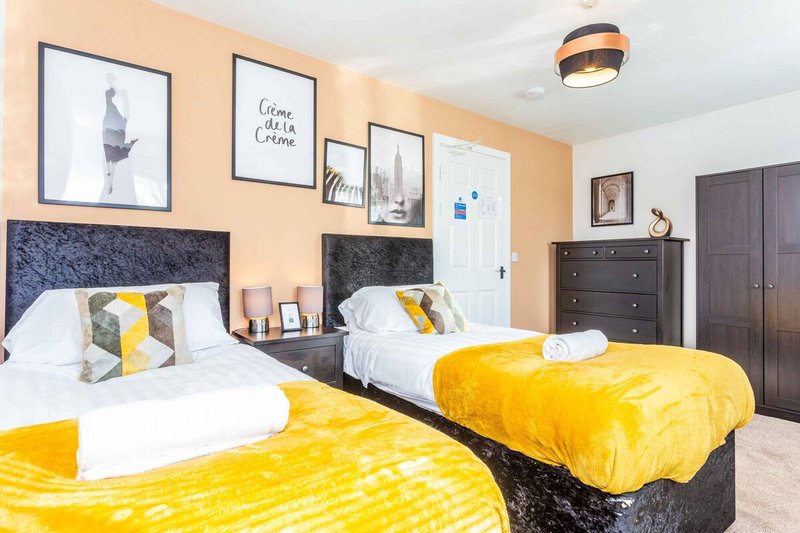 Bright bedroom with two beds, yellow bedding, framed wall art, and dark furniture