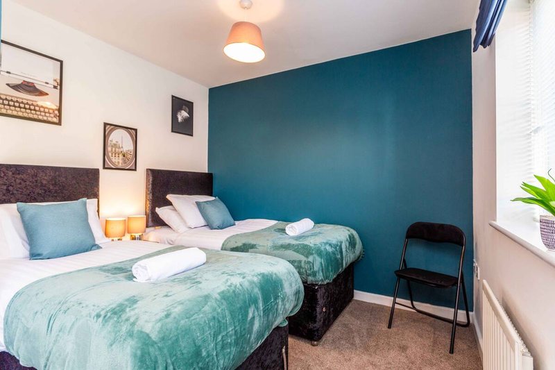 Twin bedroom with teal feature wall, two beds with green bedding, bedside lamps and framed wall art