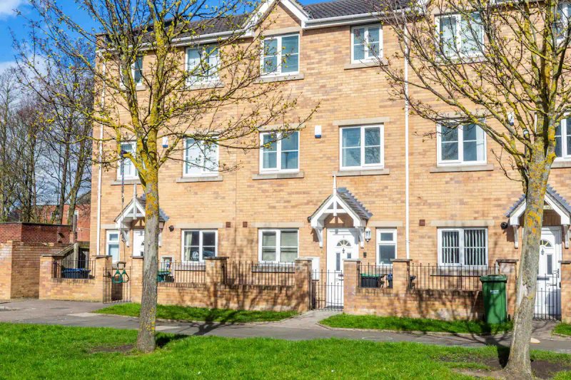 Brick townhouse exterior with multiple windows, front doors, and surrounding mature trees