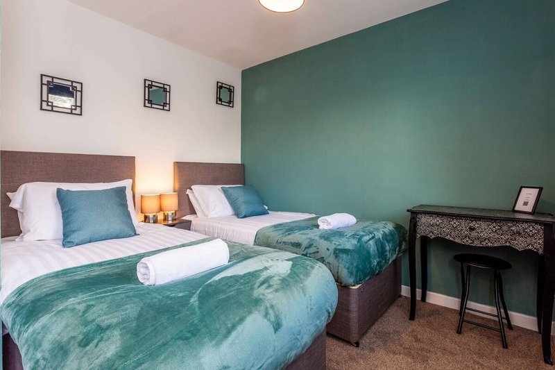 Twin bedroom with teal feature wall, two beds with matching bedding, bedside lamps and desk area