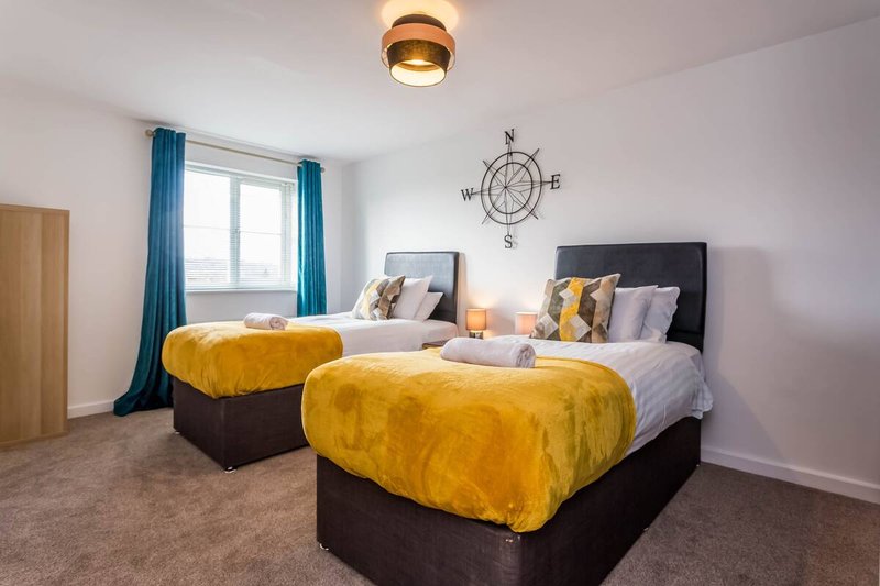 Twin bedroom with two beds, yellow bedding, dark headboards, compass wall art, window with blue curtains