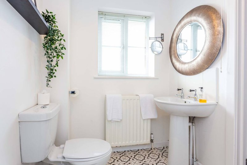 Modern bathroom with toilet, pedestal sink, circular mirror and small window