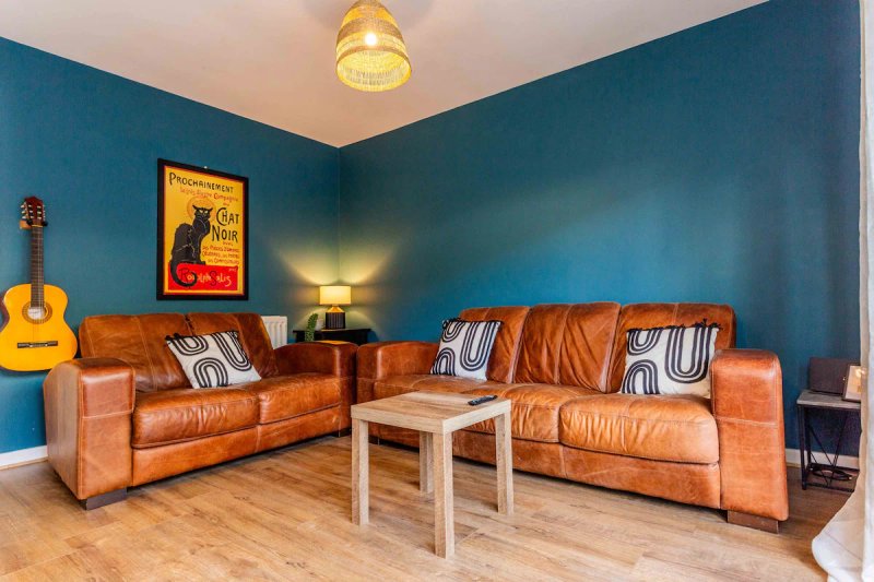 Living room with cognac leather sofas, blue walls, framed poster, acoustic guitar and ceiling light