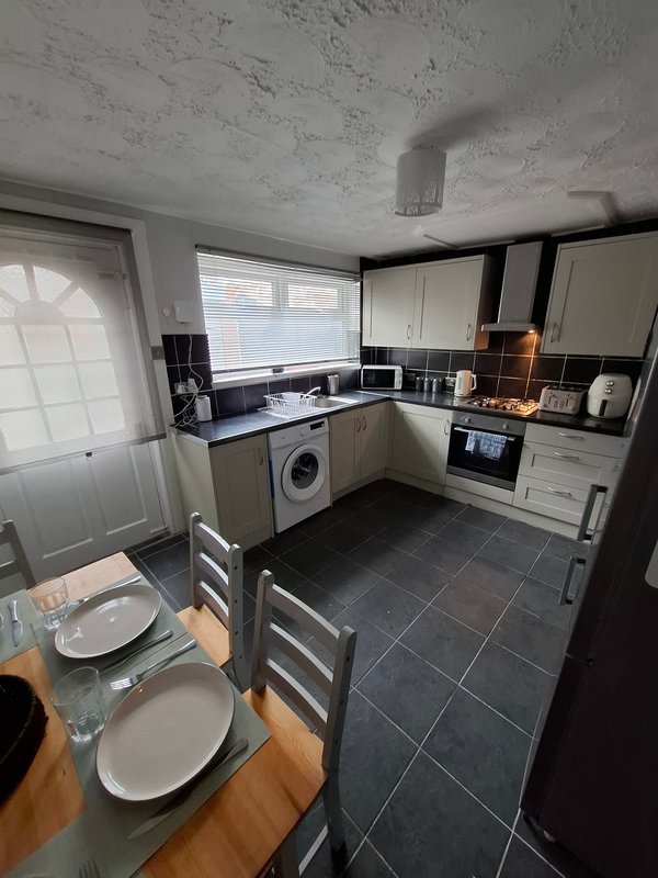 Kitchen and dining area with cream cabinets, black countertops, washing machine and dining table