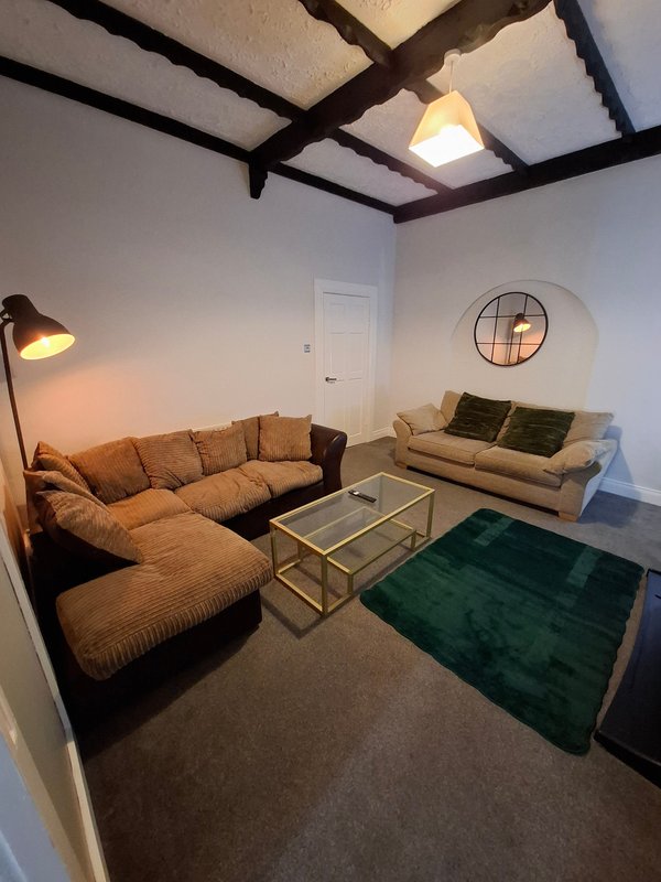 Living room with L-shaped tan sofa, glass coffee table, green rug, and exposed beam ceiling