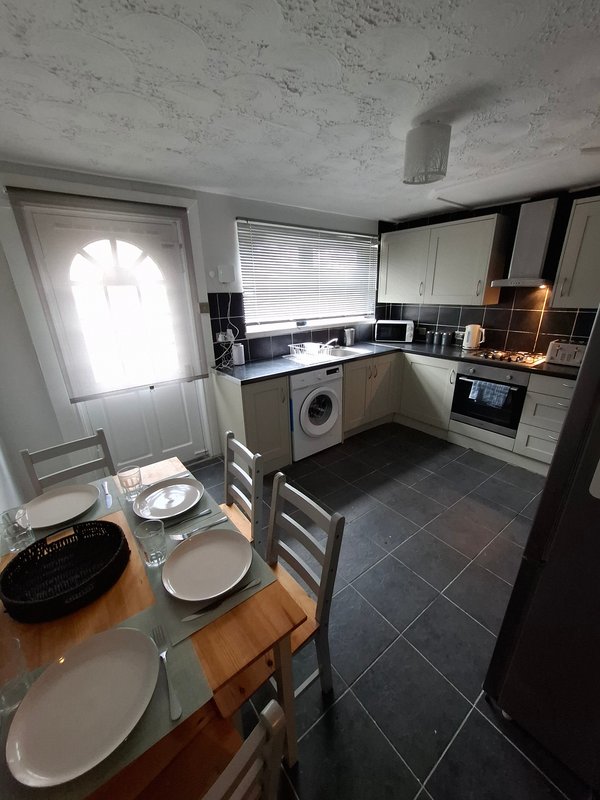 Kitchen and dining area with white cabinetry, black tile flooring, washing machine and dining table