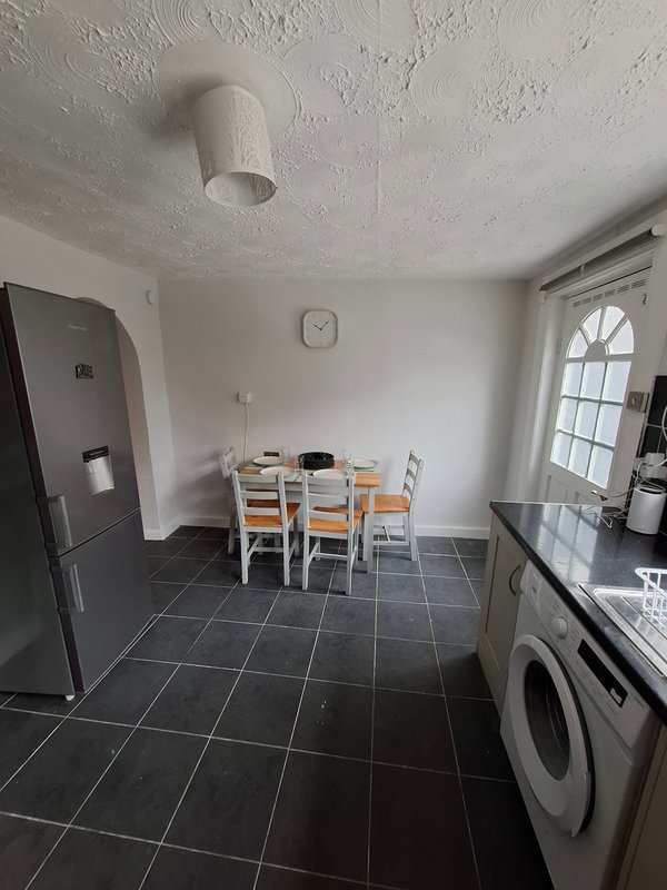 Kitchen-diner with black tile floor, dining table, chairs, fridge, washing machine and window
