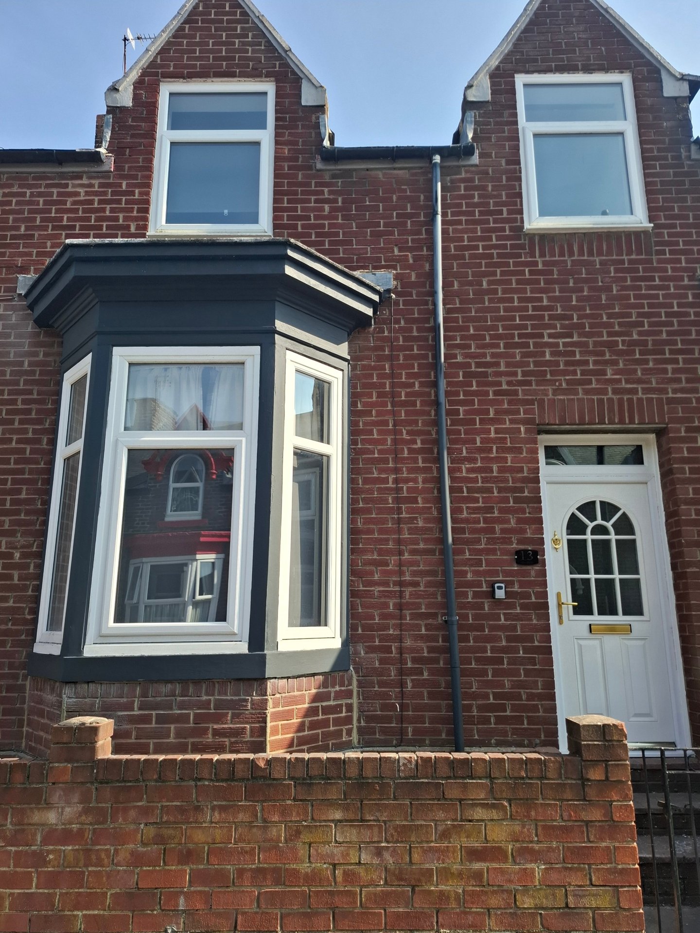 Red brick terraced house with bay window, white door frame, and dark roof
