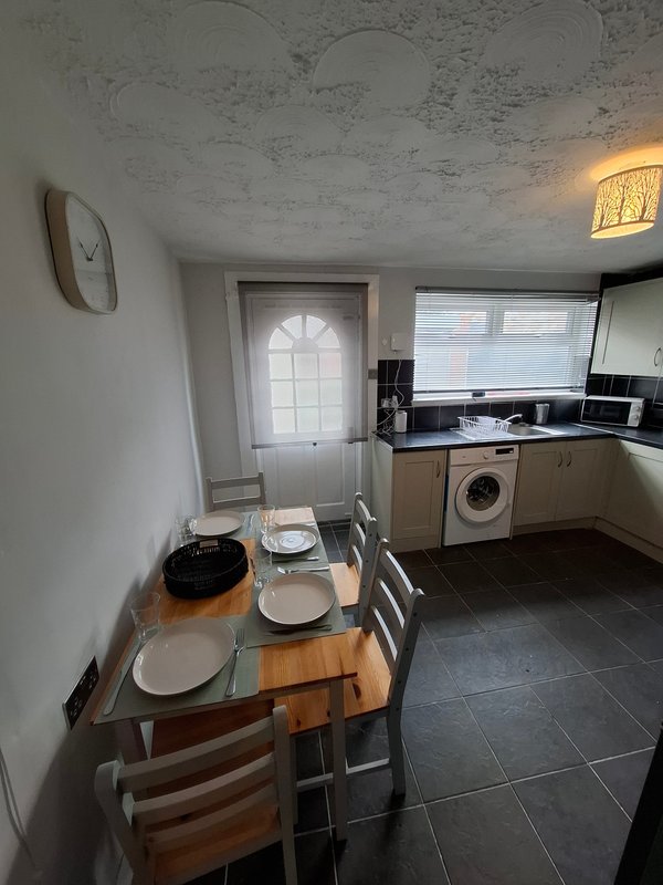 Kitchen-diner with wooden table, chairs, white appliances and door to garden