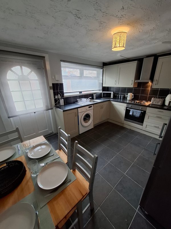 Modern kitchen and dining area with black and cream cabinetry, washing machine, and dining table set for two