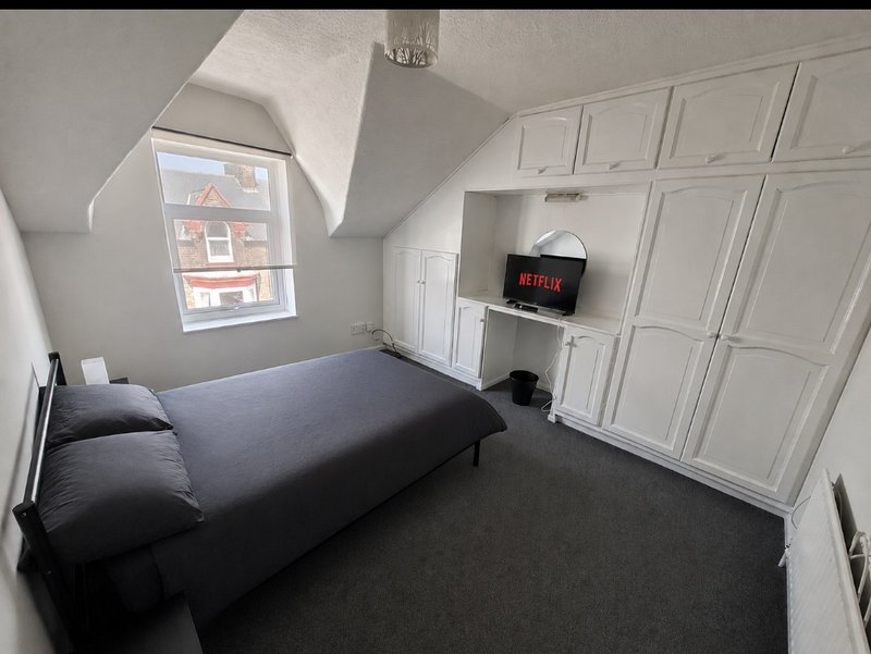 Attic bedroom with single bed, white fitted wardrobes, wall-mounted TV and sloped ceiling